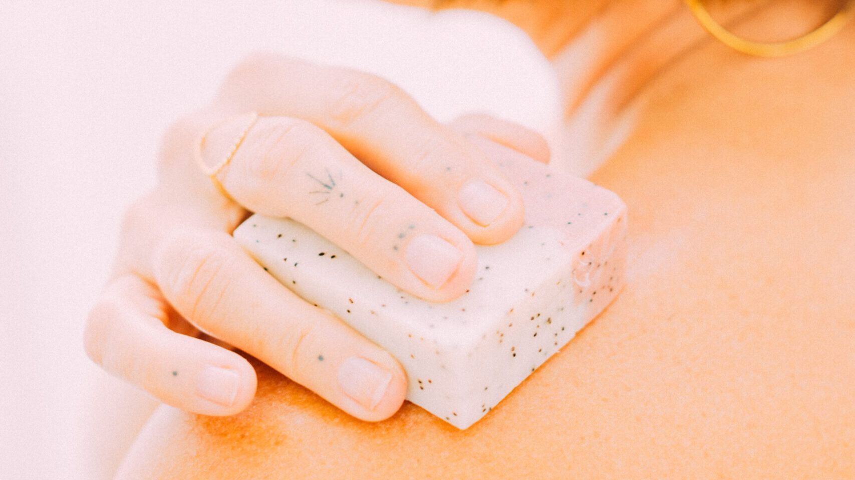 Mano aplicando jabón natural con partículas exfoliantes sobre el hombro de una persona.