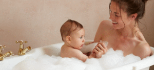 Madre bañando a su bebé en una bañera con espuma, ambos sonriendo y disfrutando el momento.