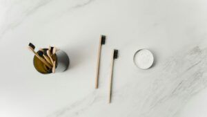Cepillos de dientes de bambú junto a un frasco con dentífrico en polvo sobre superficie blanca de mármol.